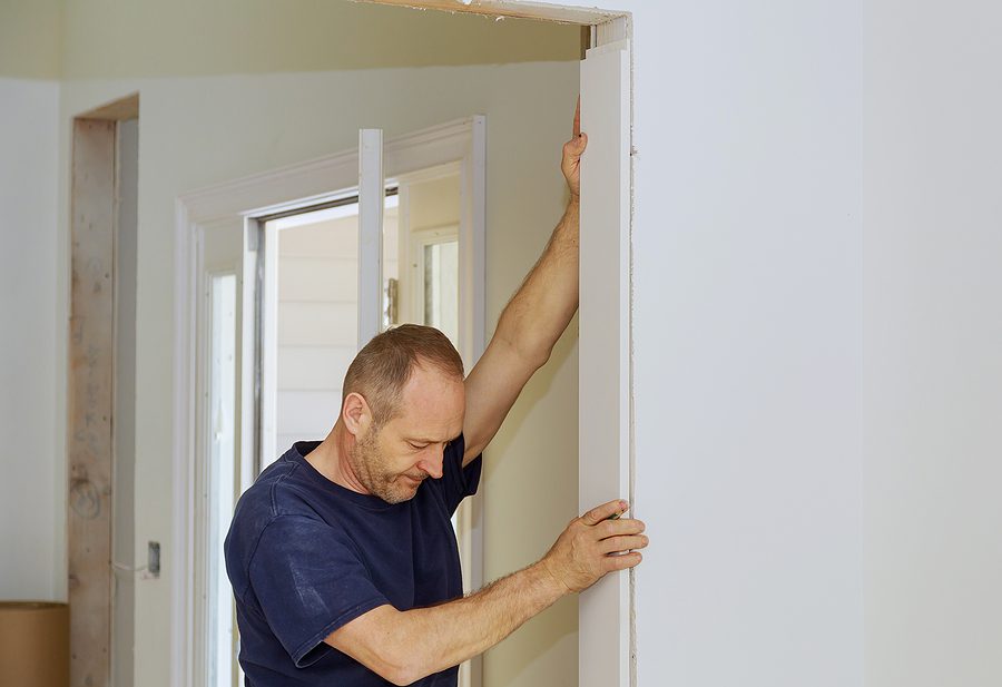 Male carpenter installing white door frame trim